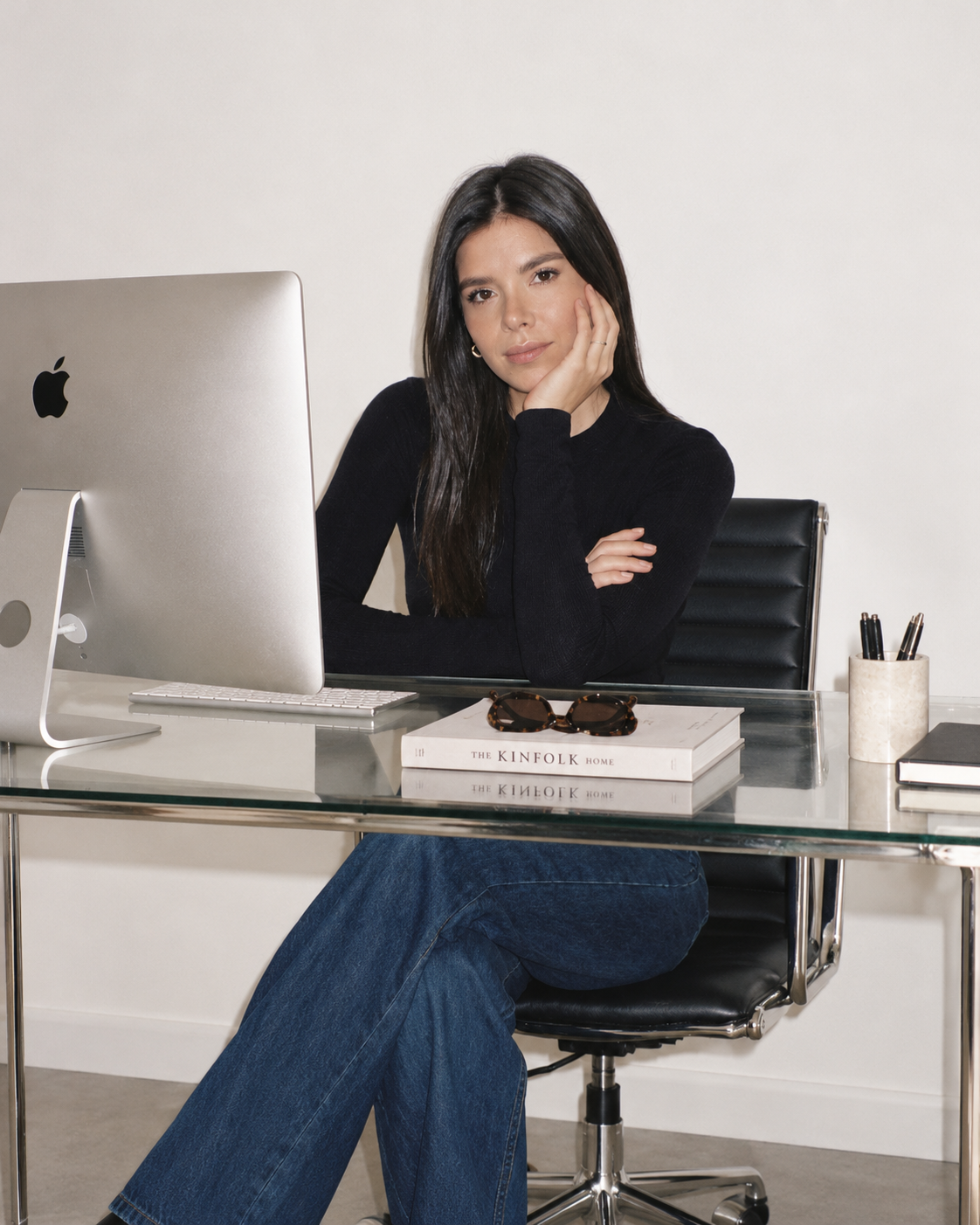 Natalia sentada en su escritorio, con un monitor y una mesa de vidrio, mirando a la cámara